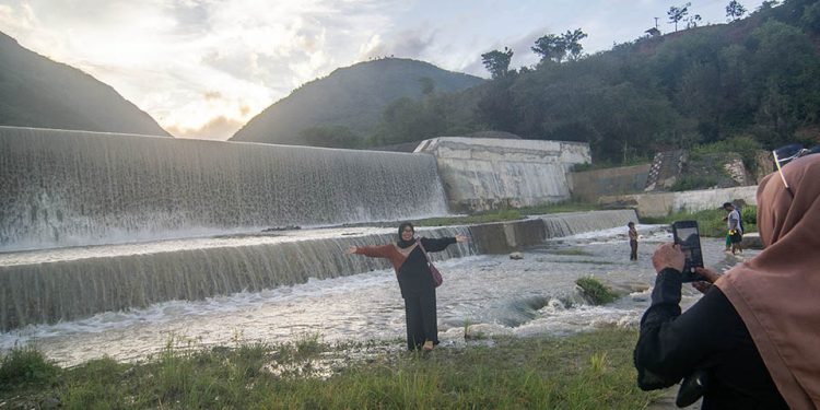 Pengunjung berfoto di depan bendungan air saat berwisata lebaran di Cek Dam Lawara, Desa Balane, Sigi, Sulawesi Tengah, Jumat (12/4/2024). Cek dam yang dibangun Balai Wilayah Sungai Sulawesi (BWSS) III dan telah direhabilitasi itu menjadi salah satu lokasi wisata lebaran yang banyak dikunjungi warga karena memiliki ari terjun dari bendungan juga menyajikan pemandangan sekitarnya yang masih alami. bmzIMAGES/Basri Marzuki