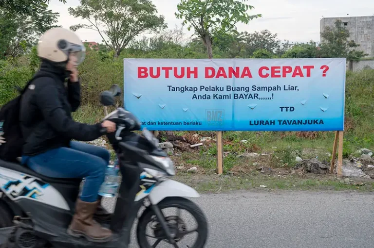 Pengendara sepeda motor melintas di depan spanduk sayembara bagi penangkap pembuang sampah liar di Kelurahan Tavanjuka, Palu, Sulawesi Tengah, Sabtu (19/4/2025). (bmzIMAGES/Basri Marzuki)